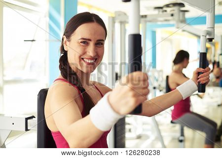 Young beautiful smiling girl in sportswear is working out on butterfly machine in gym