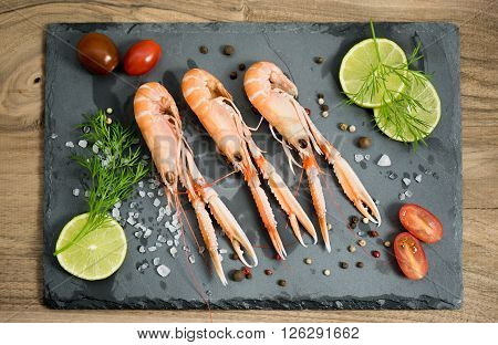 Scampi, lemon lime, white salt and cherry tomatos on the black rock.