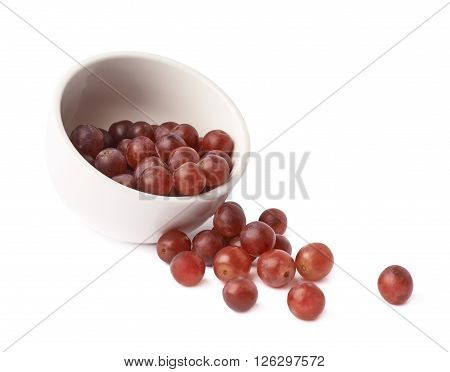 Dark red grapes spilled out of the white cermic bowl, composition isolated over the white background