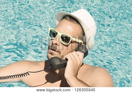 Close up of a young man using a retro styled handset in the swimming pool