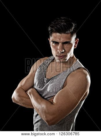 young attractive sport man with big and strong athletic body posing with folded arms wearing sweaty singlet looking cool and showing attitude isolated on black background