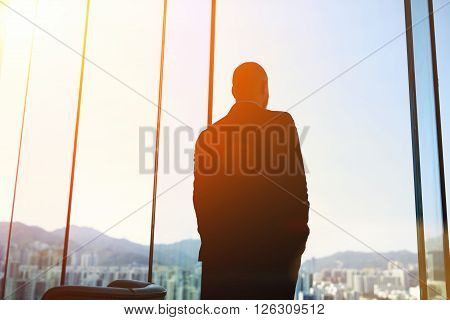 Silhouette of man managing director is examining the challenges the company after the refusal of investors in financing while standing in evening time against office window background with copy space