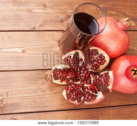 Pomegranate Punica granatum fruit next to the tall glass full of red juice, composition placed over the wooden boards surface