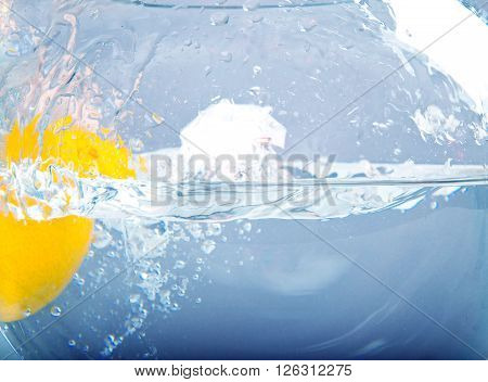 Lemon is dropped into water splash on white