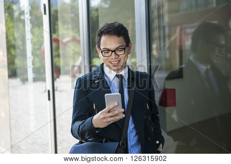 Young asian business man looking at mobile phone outside on city street near building