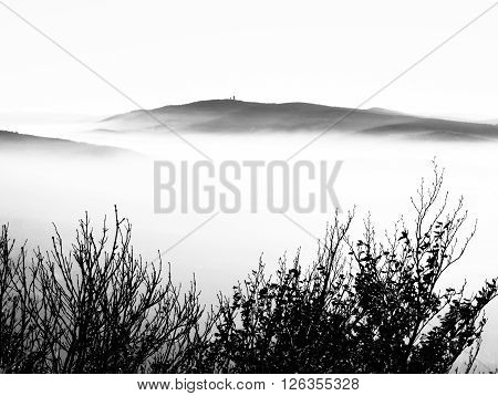 Cerchov Mountain above clouds in autumn inversion weather, Czech Republic. Black and white image.