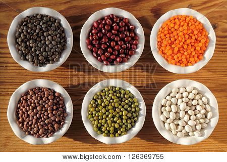 Colorful beans and lentils in ceramic bowls on a wooden background.