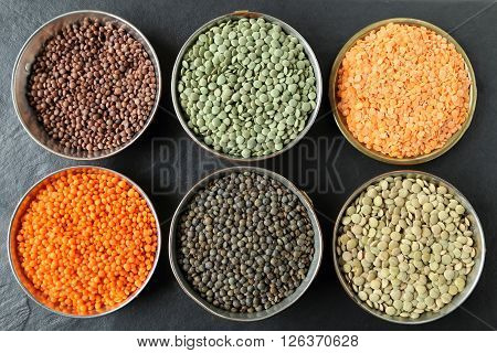 Colorful lentils in metal bowls on a dark background.