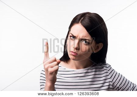 Do not do it. Gloomy distempered serious girl holding her finger up and making commands while standing isolated on grey background