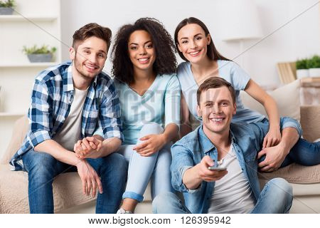 Choose another channel. Pleasant handsome guy holding remote control and watching TV  together with his friends