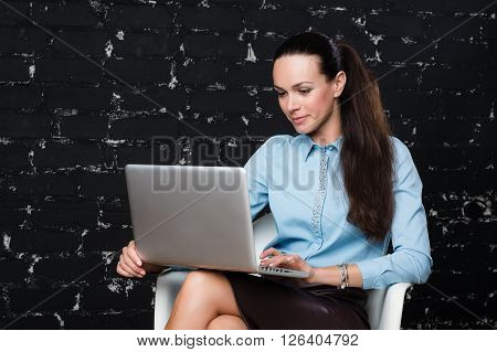 Russian business lady looking to the laptop on the black brick background for use e.g. in collages, presentation