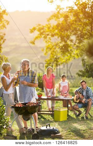 smiling grandparents drinking wine and enjoying picnic with family
