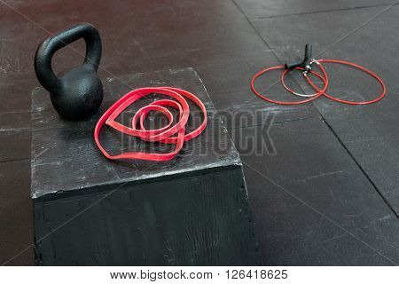 Black kettle bell and red fitness band on a black jump box, red jump rope on the floor
