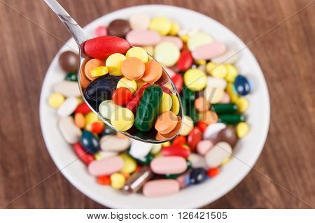 Pills on teaspoon and capsules or supplements for therapy in background on plate concept of treatment