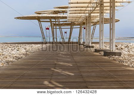 Wooden dock with sunshade leading to the sea surrounded with natural boulders with heavy shades from parasol
