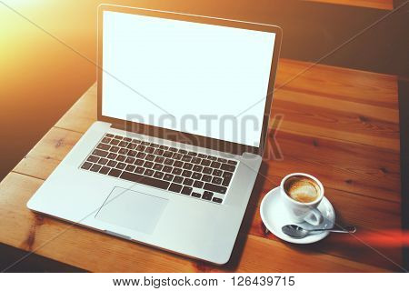 Portable laptop computer and cup of coffee lying on a wooden table in cafe bar interior open net-book with copy space screen for your advertising content or text message remote work via internet