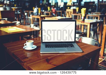 Open laptop computer and cup of coffee lying on a wooden table in cafe bar interior portable net-book with copy space screen for your information content or text message distance work via internet