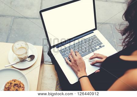 Back view of business woman is typing text on laptop keyboard during work break in cafe. Female freelancer is working on net-book with mock up blank copy space screen for your text message or concept