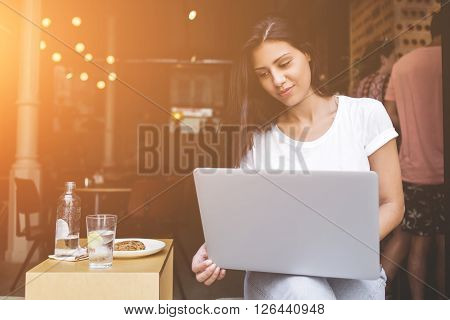 Portrait of a charming latin woman having video call conference on her net-book during lunch break in modern coffee shop. Young female student using laptop computer for learning while sitting in cafe