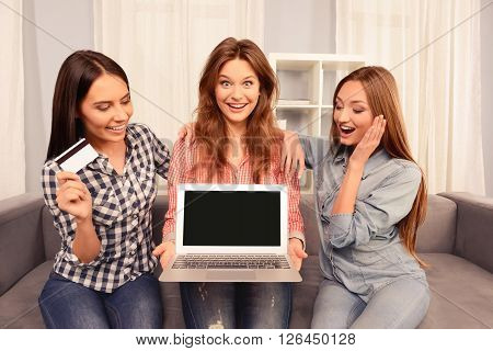 Three Happy Women Sitting On Sofa And Showing Laptop And Bank Card