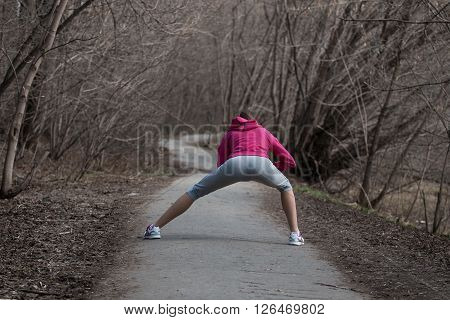 Beautiful young woman doing stretching exercises before running in the park
