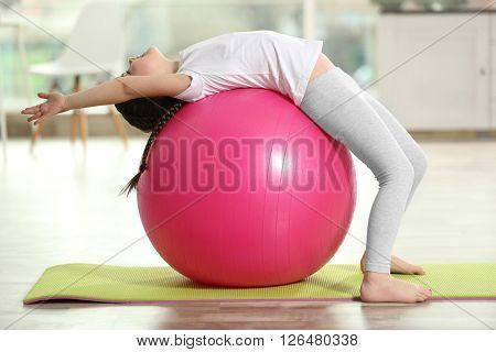 Little cute girl doing exercises with ball on a mat indoor