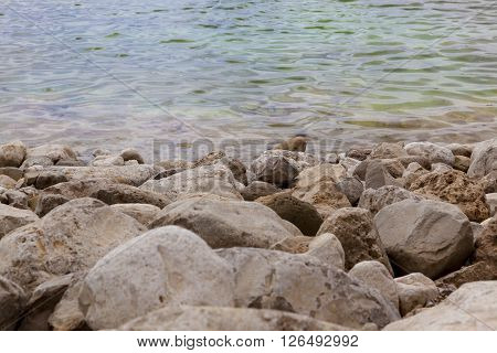 White yellow grey natural boulders with salt levee on blue water edge of Dead Sea with ripples
