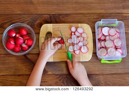Child cuts vegetables for salad using kitchen knife. Children hands holding a knife and a radish. Vegetables for salad. Top view