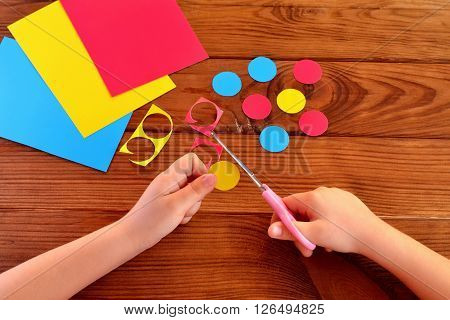 Children hands holding the scissors and paper and cut out the circle. Sheets of paper, paper circles on a brown wooden background