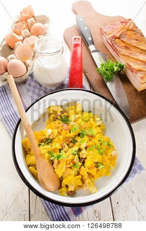 scrambled eggs with fat smooked bacon parsley and milk in a pan