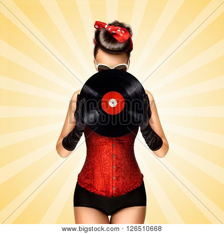 Vintage photo of glamorous pinup girl wearing long gloves and dressed in a red sexy corset hiding behind LP vinyl record on colorful abstract cartoon style background.