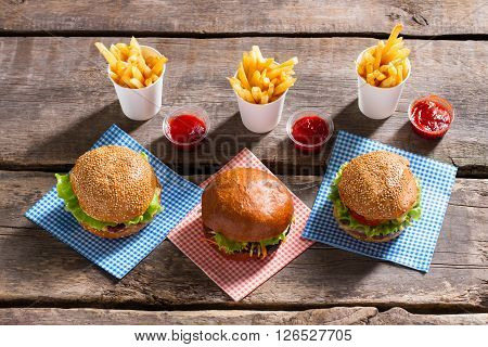 Burgers with ketchup and fries. Hamburgers and sauce on table. Soft buns with juicy meat. Enjoy your food.