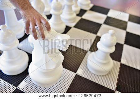 Hand moving the white knight on a giant chess game