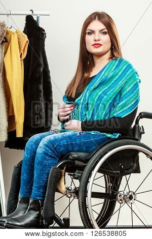 Real people disability and handicap concept. Teen girl handicapped woman sitting on wheelchair choosing clothes in wardrobe or looking for some clothes in shop