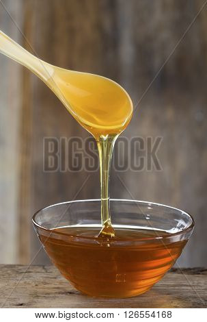 Honey pouring from drizzler into the bowl on wooden table