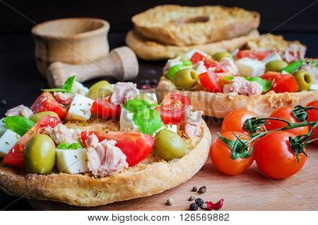 Classical frisella tomato, cheese mozzarella, tuna and olives. Italian starter friselle. Dried bread called freselle on wooden board with tomatoes cherry. Italian food. Healthy vegetarian food.