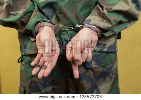 Young man in handcuffs wearing camouflage uniforms in the room.