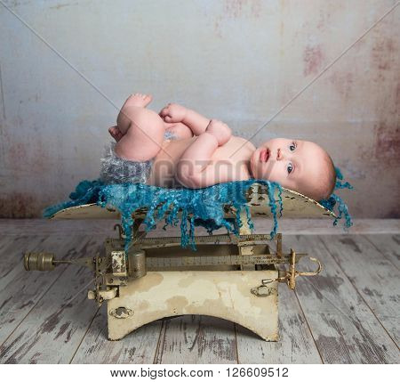 cute little baby with legs up lying on child scales on wooden floor