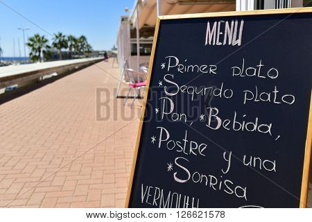 closeup of the chalkboard of a restaurant in a coastal city in Spain, with a generic menu including a starter, a main course, bread, beverage, dessert and a smile, written in spanish