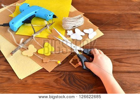 Child holds the scissors and cut out the felt flower. Scissors, hot glue gun, sheets of felt, decorative pendant with felt butterflies and flowers