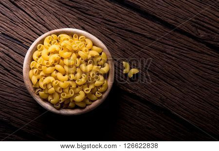Raw pasta in wooden bowl on wood background