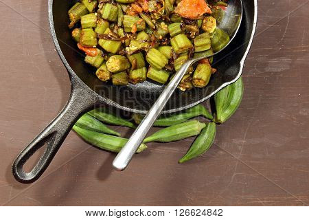 A cast iron pan with cooked Bhindi masala with copy space on a moody background.