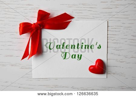 Blank present card with ribbon bow and small heart on wooden background