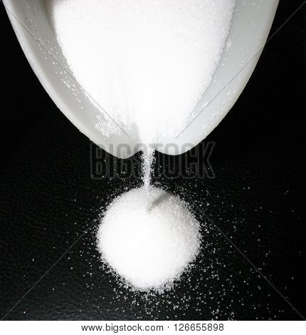 White sugar grains run out of a bowl on black background