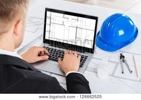 Male Architect Analyzing Blue Print On Computer Over Blue Print In Office