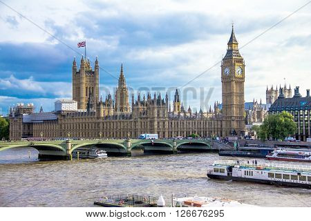 LONDON UK - JUNE 6 2015: Tourist pleasure boat on the River Thames at summer evening on cityscape of London  with houses of Parliament, Big Ben , Westminster Abbey and Westminster bridge and cloudy sky background