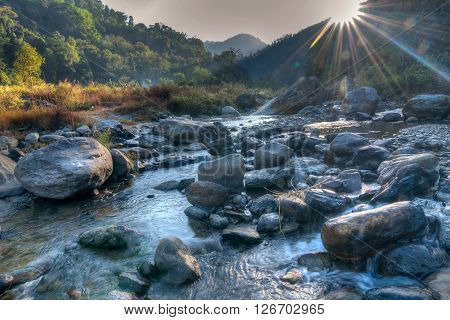 Beautiful Reshi River water flowing on rocks at dawn Sikkim India - sun rays at the background falling on water making spectacular view