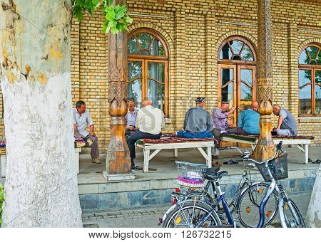 KOKAND UZBEKISTAN - MAY 6 2015: The elderly men spend their time playing cards and sitting on the trestle-beds at the summer terrace of traditional teahouse on May 6 in Kokand.