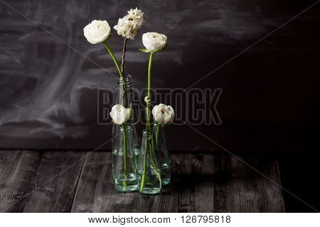 Four white buttercups and blossom apple in small glass bottles standing in the dark wooden floor with blackboard in the background