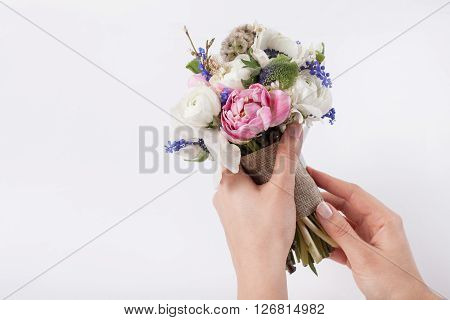 Two hands are making a beautiful pastel bouquet from pink tulips violet grape hyacinths white anemones violet veronica and white buttercups on white background